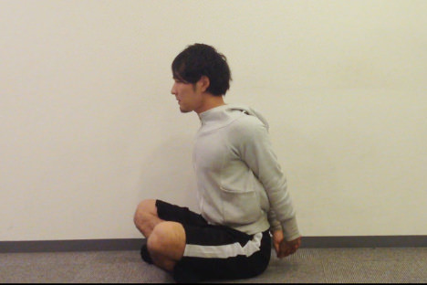 身体の後ろで両手のひらを組み、真下に向かって腕をピンと伸ばす男性