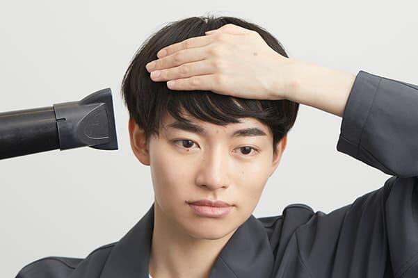 ドライヤーをあて前髪を抑える男性画像