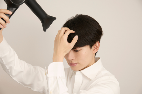 前髪にドライヤーをあてる男性の画像