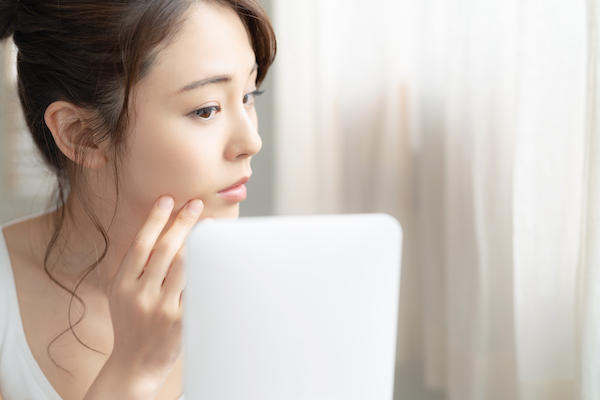 女性が自分の肌を鏡で見ている様子の画像。