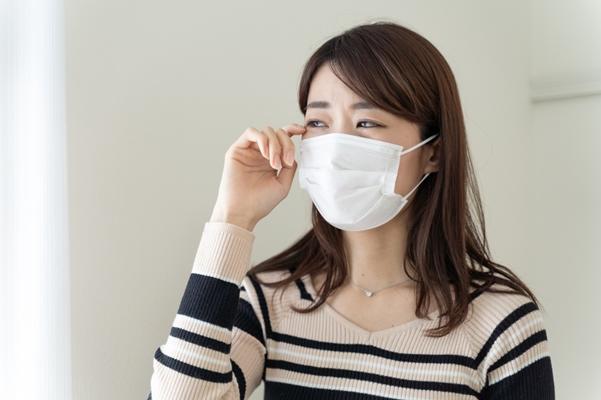 マスクをつけた女性が目を痒そうにしている写真。