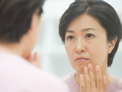 鏡をのぞき込み、濃いシミに悩む不安そうな表情の女性